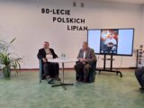 Spotkanie historyczne, grupa ludzi słucha prelekcji. Widać ekran multimedialny oraz ścianę z napisem "80-lecie polskich Lipian"